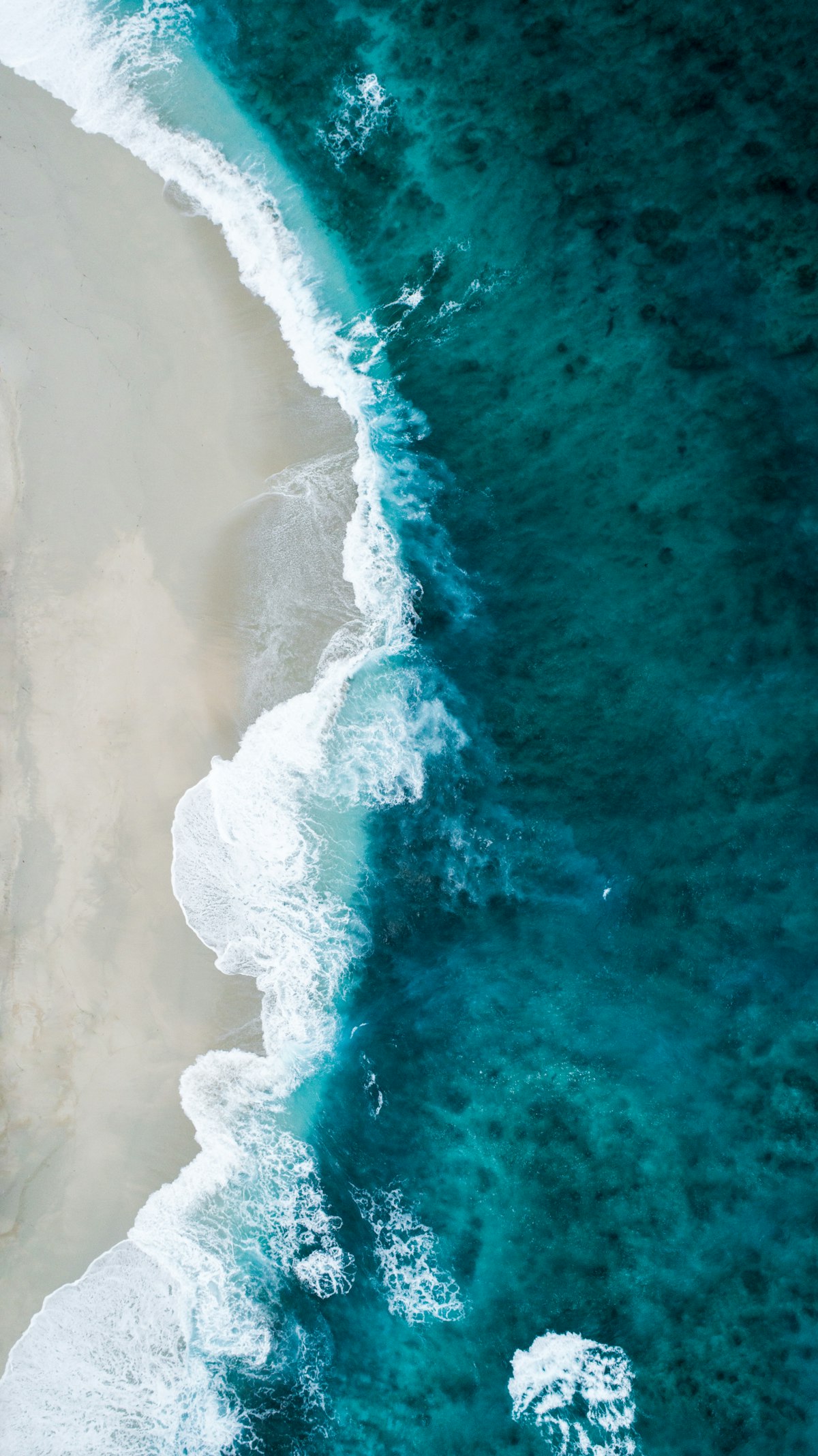Aerial view of turquoise waves meeting white sand